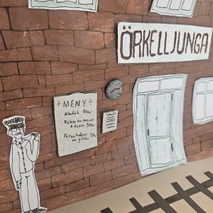 Detalj av stationshuset med men, stins och stationsskylt